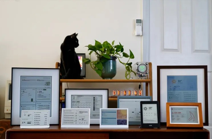 – Mehrere E-Ink-Displays mit Wetter-, Kalender- und GitHub-Dashboards stehen vor einem Regal mit Pflanze und schwarzer Katze.